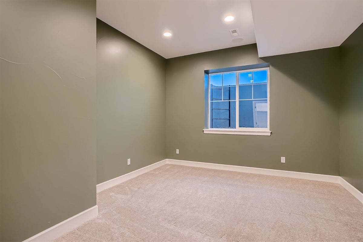 Lower-level bedroom with forest green walls, carpet flooring, and a sliding window in a Sheffield Homes home in Superior, CO