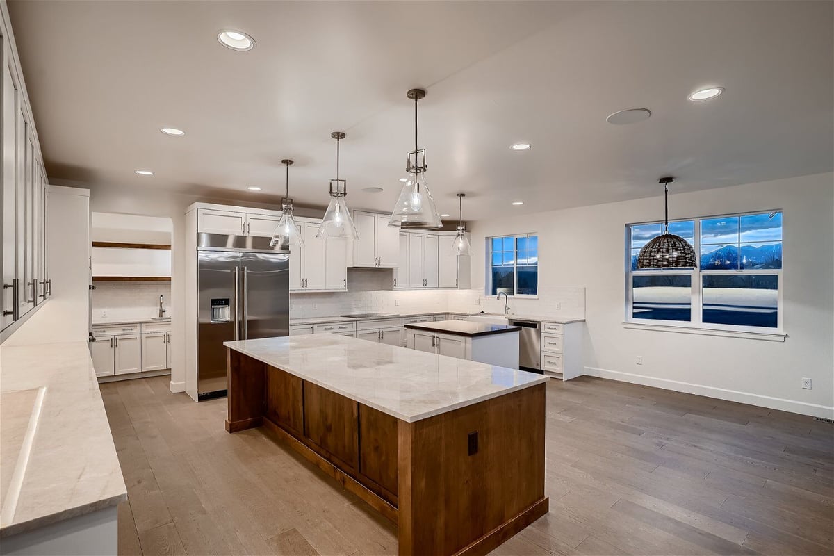 Modern open kitchen with elegant pendant lighting, white cabinetry, and appliances in a Sheffield Homes home in Superior, CO