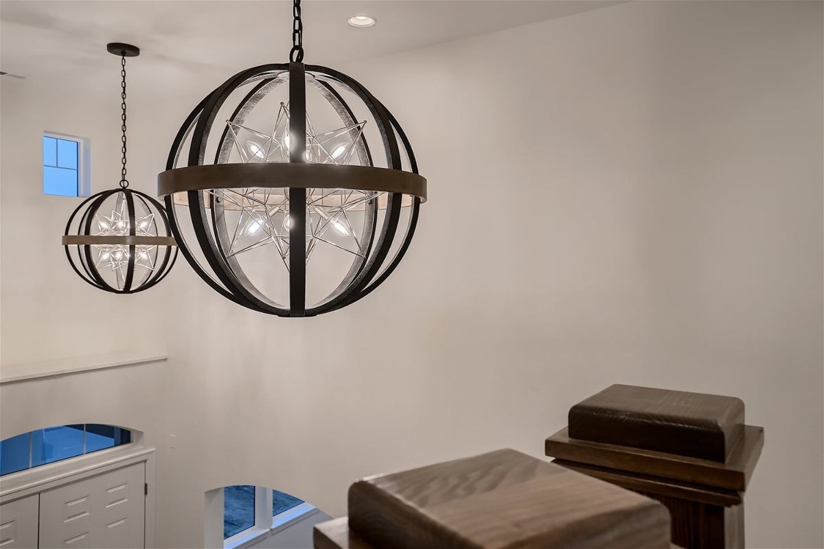 Two fancy chandeliers with lit-up bulbs viewed from the staircase railing in a custom Sheffield Homes home in Superior, CO