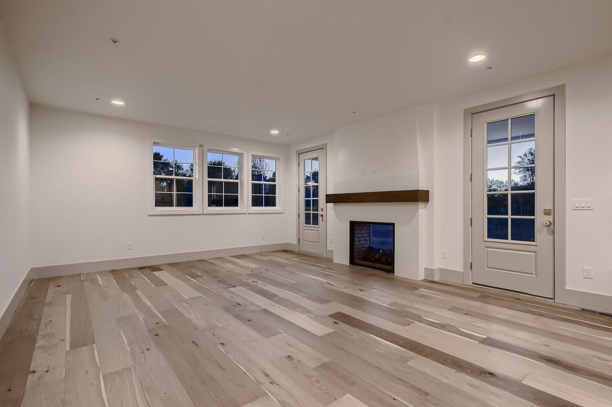 Living room with vinyl flooring, a wall-mounted fireplace, a door, and windows in a Sheffield Homes home in Westminster, CO