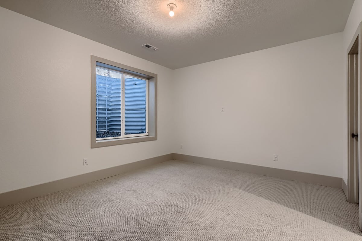 Lower-level bedroom with carpet flooring, white walls, and a large window in a Sheffield Homes home in Westminster, CO