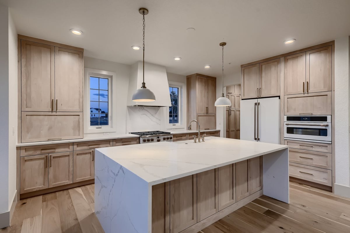 Open kitchen with a central island, contemporary light fixtures, and wooden cabinetry in a Sheffield Homes home in Westminster, CO