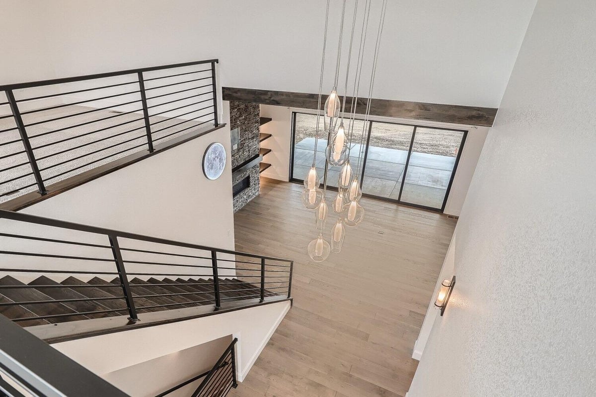 A pendant chandelier is viewed from the upper floor stairways with metal railings in a Sheffield Homes home, Westminster, CO