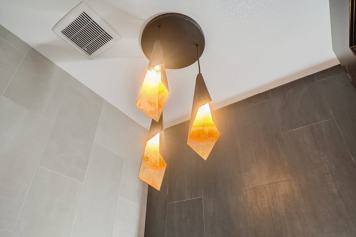 Bottom-up shot of a fancy pendant chandelier with three lit-up lamps in a custom home by Sheffield Homes in Westminster, CO