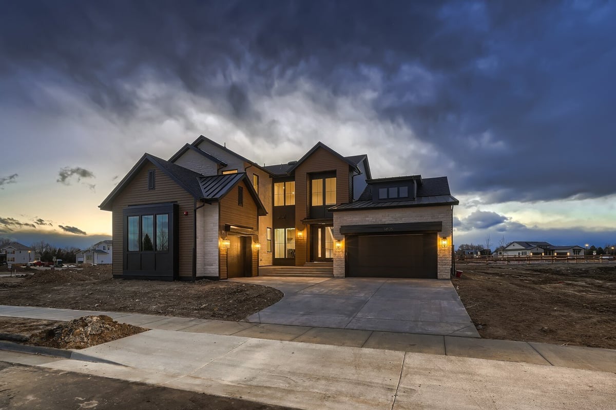 Low-light exterior front view of a large custom home and a garage with a paved walkway, by Sheffield Homes in Westminster, CO