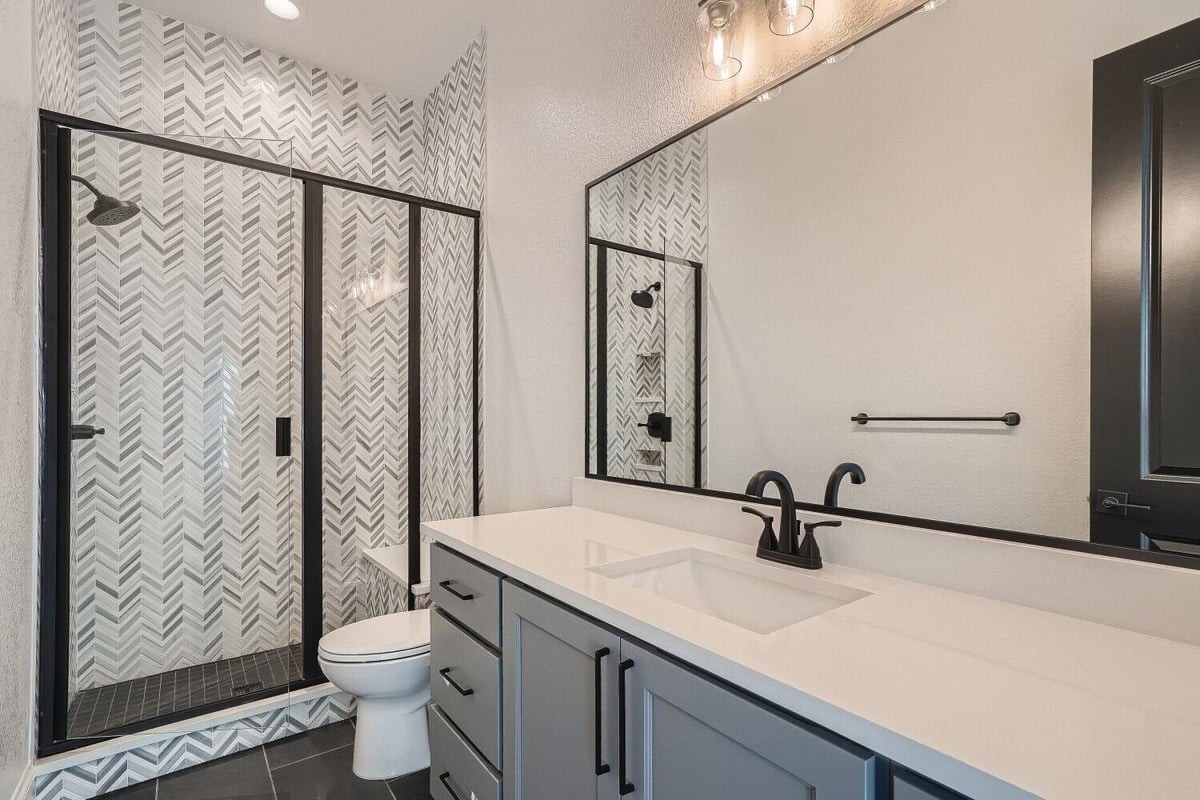 Modern bathroom featuring a stylish vanity, a toilet, and a glass-enclosed shower room by Sheffield Homes in Westminster, CO