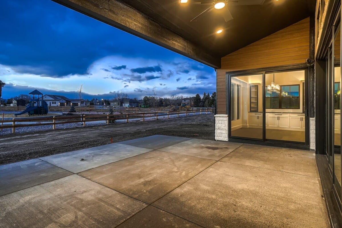 Outdoor patio with a smooth floor and elegant lighting visible through the sliding door, by Sheffield Homes, Westminster, CO