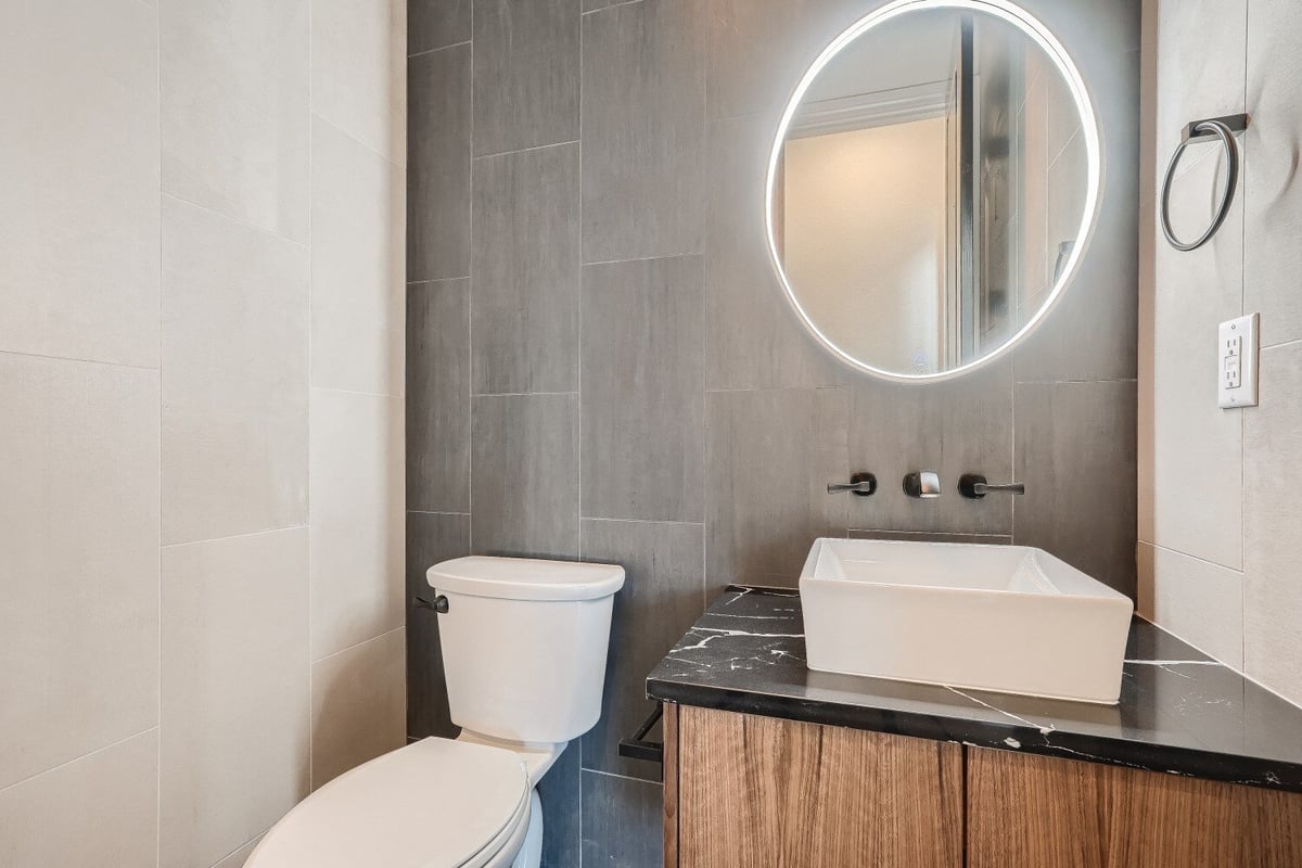 Powder room featuring a sink with a lit-up mirror and a toilet seat, in a custom home by Sheffield Homes in Westminster, CO