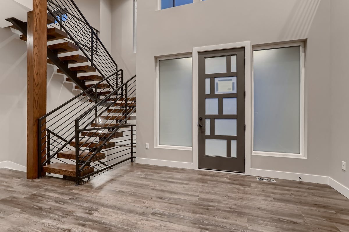 Customized wooden staircase and main access door in the foyer of a custom home by Sheffield Homes in Westminster, CO