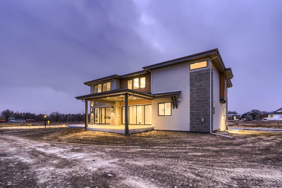 Low-light exterior rear view of a custom home with elegant lighting and a backyard by Sheffield Homes in Westminster, CO