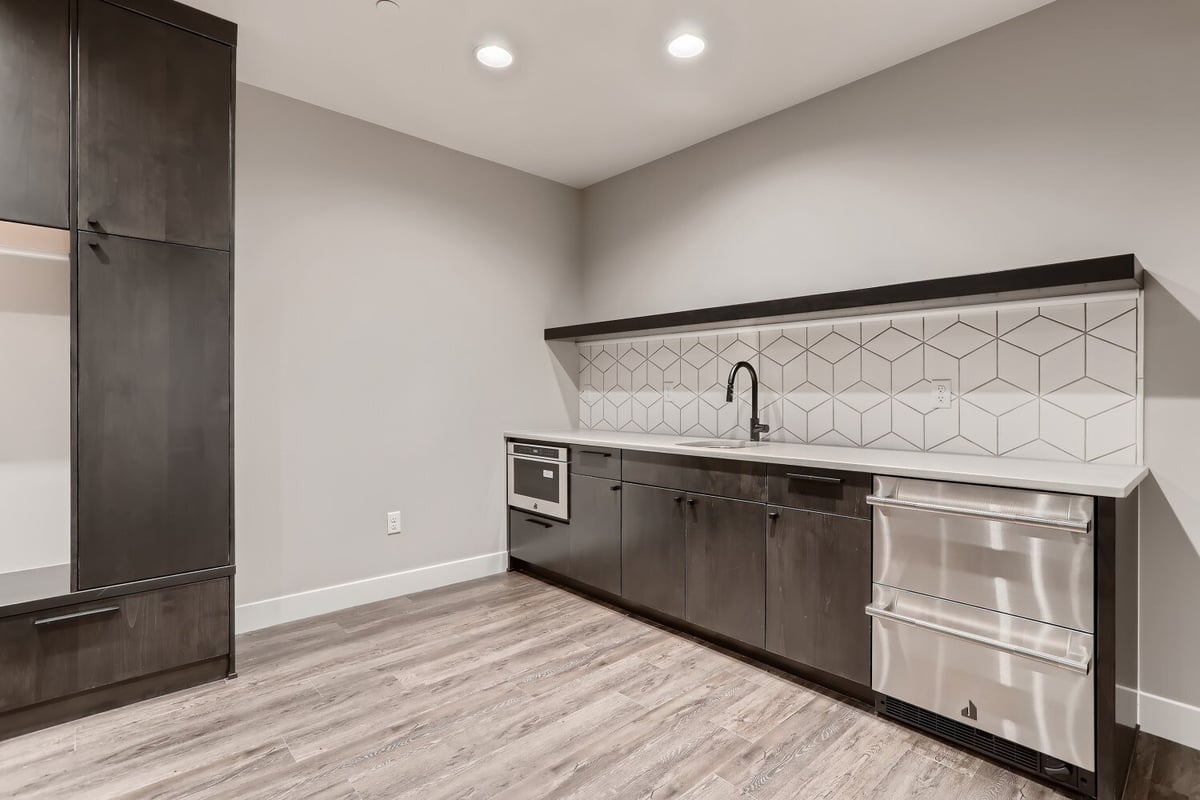 Lower-level bar with a sink and faucet, and a large closet against the left wall, by Sheffield Homes in Westminster, CO