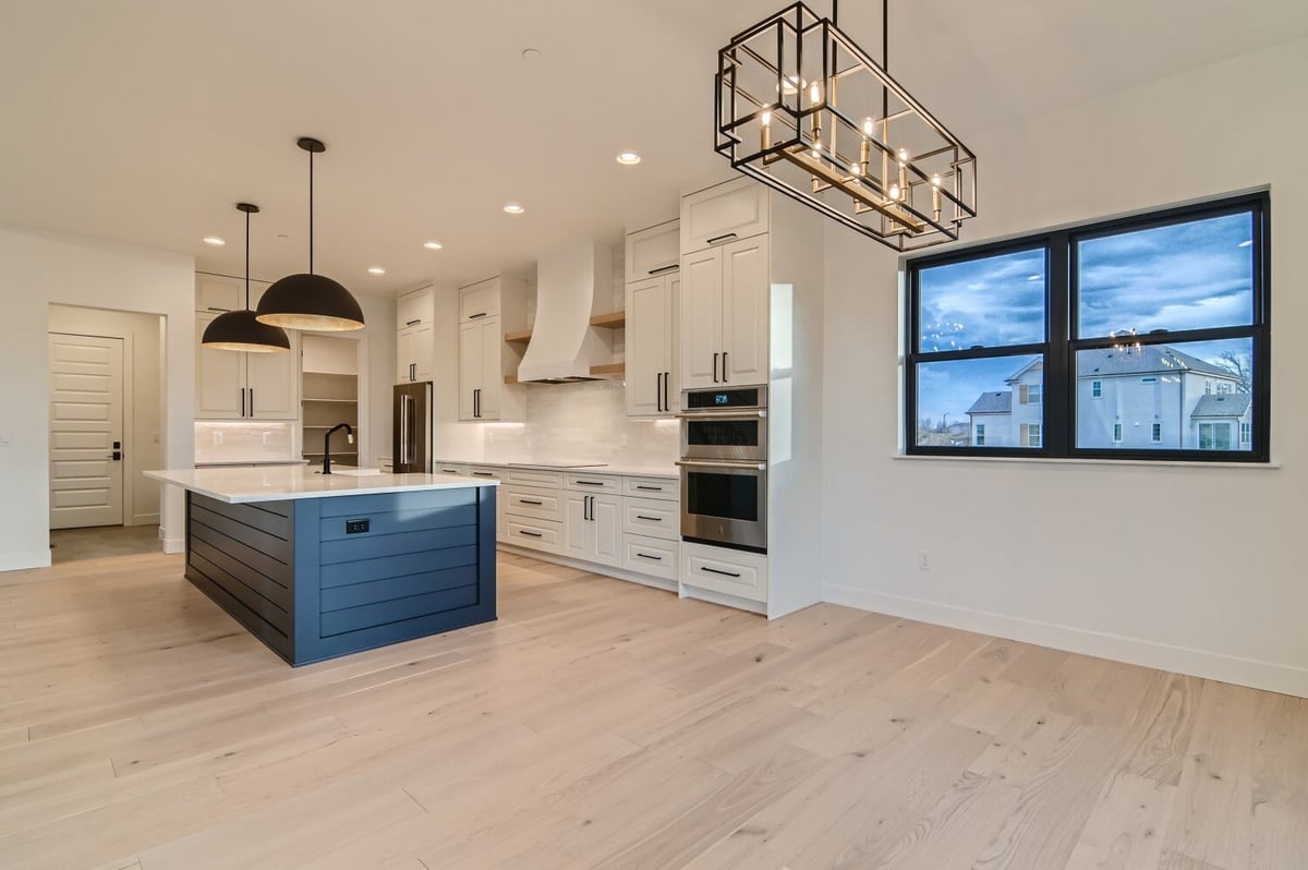 Dining room with a bright chandelier and a window next to the open kitchen in a Sheffield Homes home in Westminster, CO