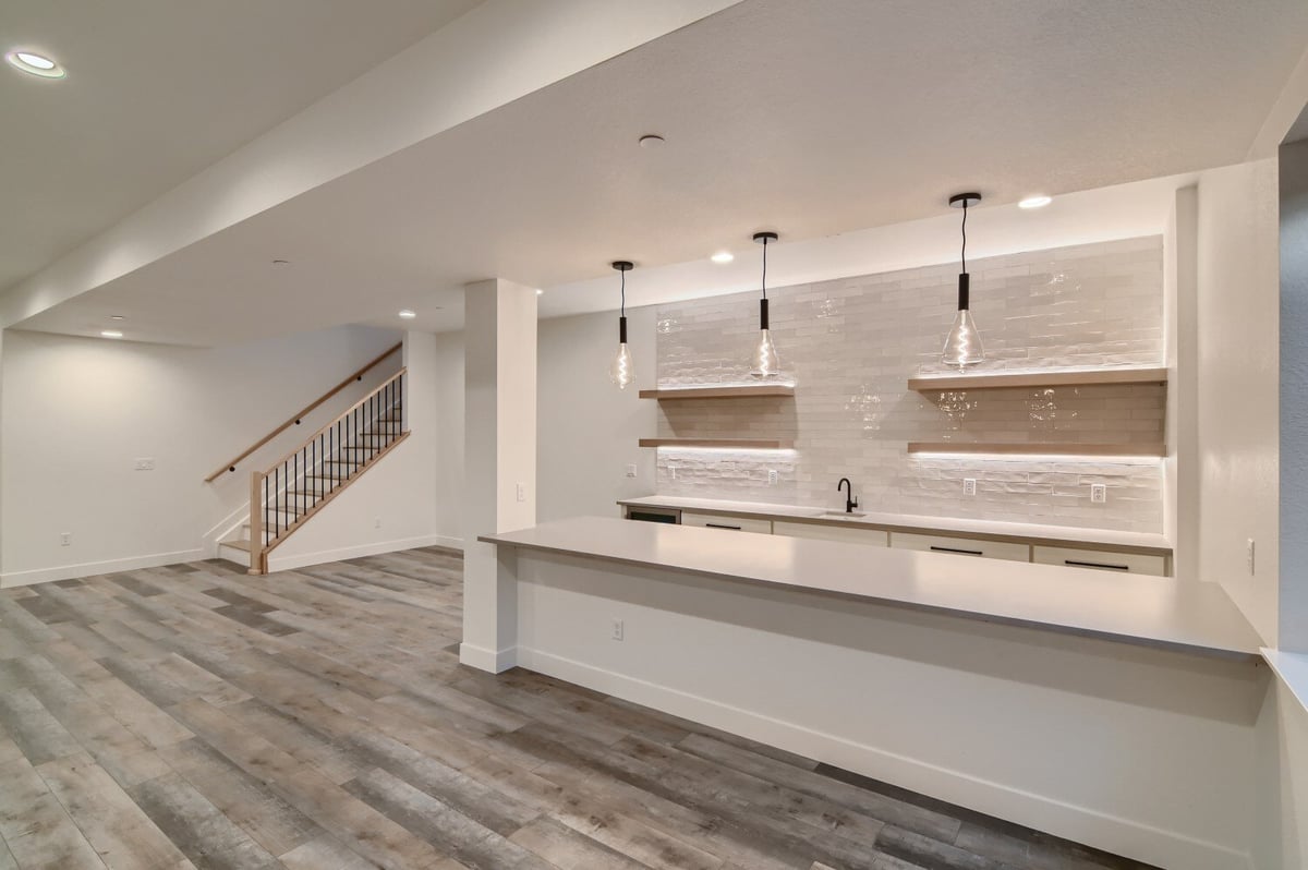 Kitchen with two counters and elegant light fixtures, with stairs in the background, by Sheffield Homes in Westminster, CO