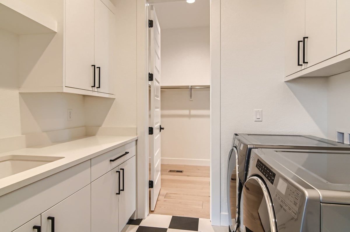 Laundry room with washing machines and sleek white cabinetry for storage in a home by Sheffield Homes in Westminster, CO