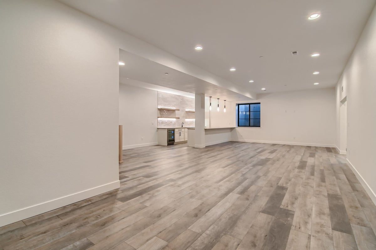 Lower-level family room with vinyl flooring for recreational activities and a kitchen by Sheffield Homes in Westminster, CO