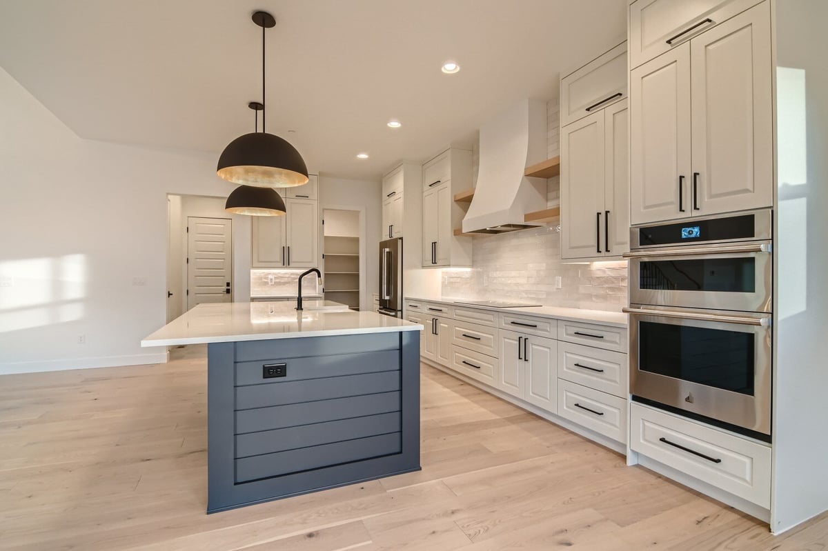 Modern island with a marble countertop, wooden base cabinets, and overhead lights, by Sheffield Homes in Westminster, CO