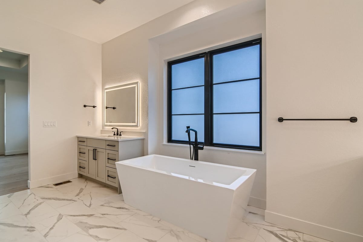 Primary bathroom featuring a bathtub beside a modern vanity with a glowing mirror in a Sheffield Homes home, Westminster, CO