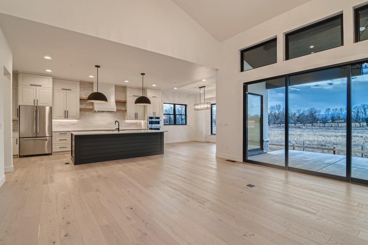 Spacious living room with an open kitchen and three large doors offering outside views by Sheffield Homes in Westminster, CO