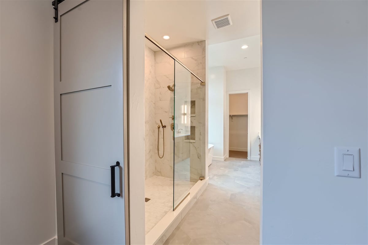 Bathroom with a white access door and a shower area with glass-enclosed door, by Sheffield Homes in Westminster, CO