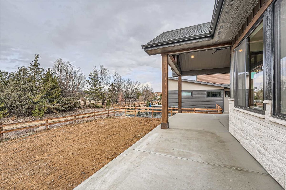 Custom patio with a hood supported by wooden pillars, offering backyard views, by Sheffield Homes in Westminster, CO