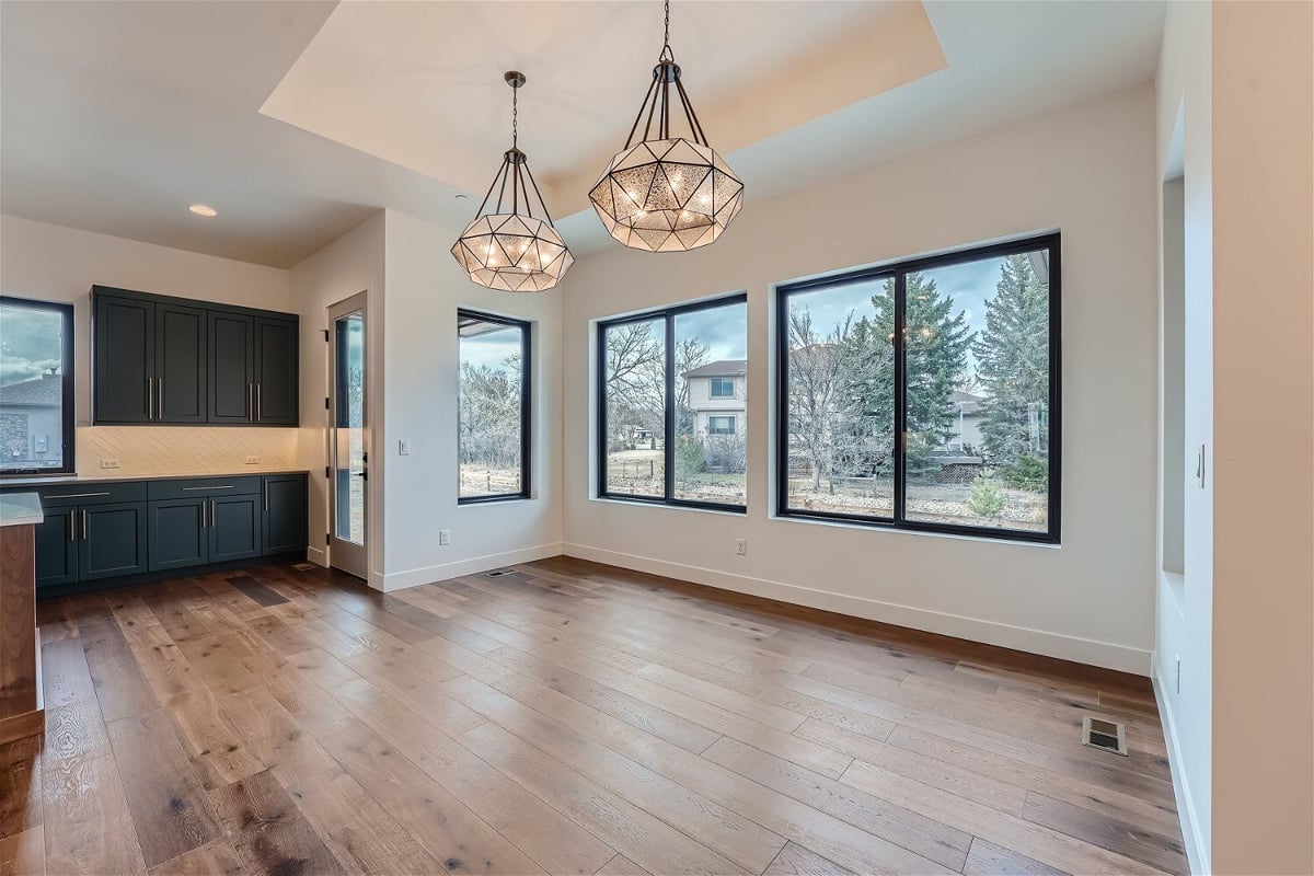 Dining room with twin lit-up chandeliers adjacent to the kitchen with black cabinets, by Sheffield Homes in Westminster, CO