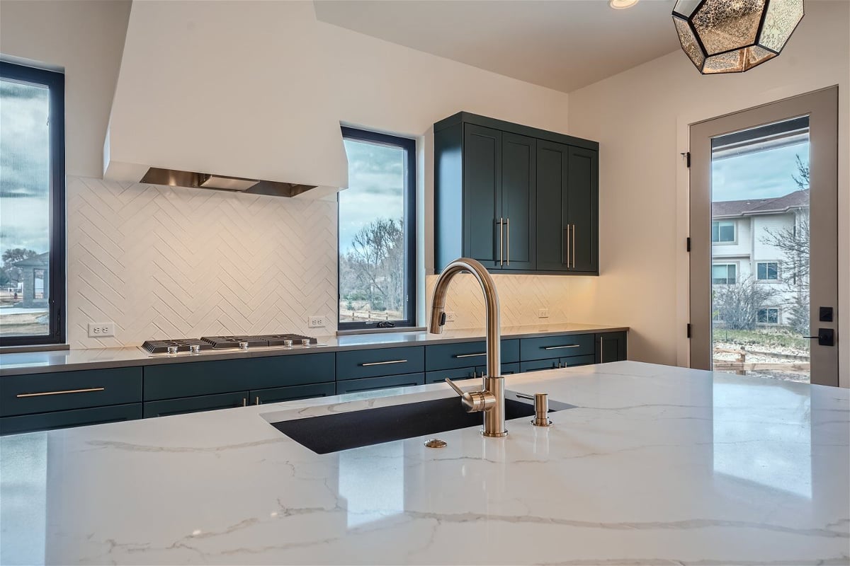 Kitchen island with a sleek countertop, golden faucet, and an extractor hood behind, by Sheffield Homes in Westminster, CO