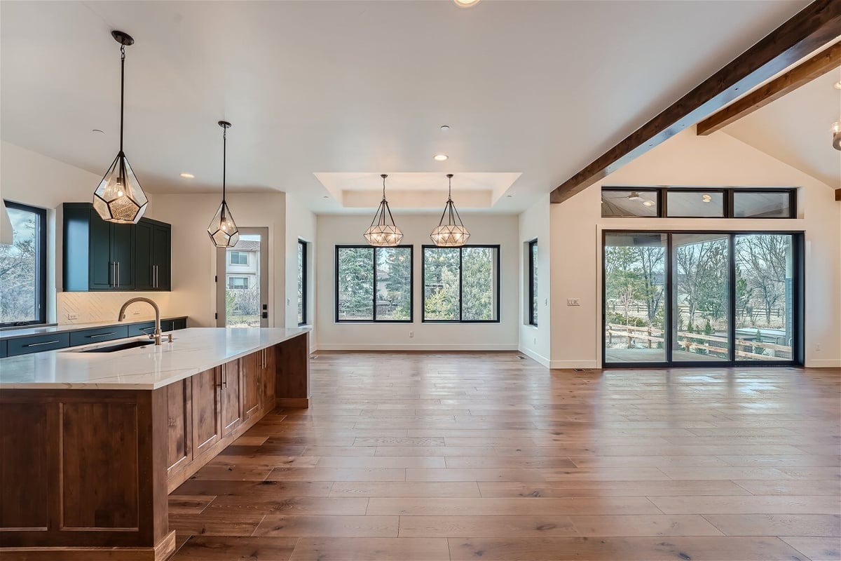 Open kitchen with a central and rear counter, and multiple glowing chandeliers overhead by Sheffield Homes in Westminster, CO