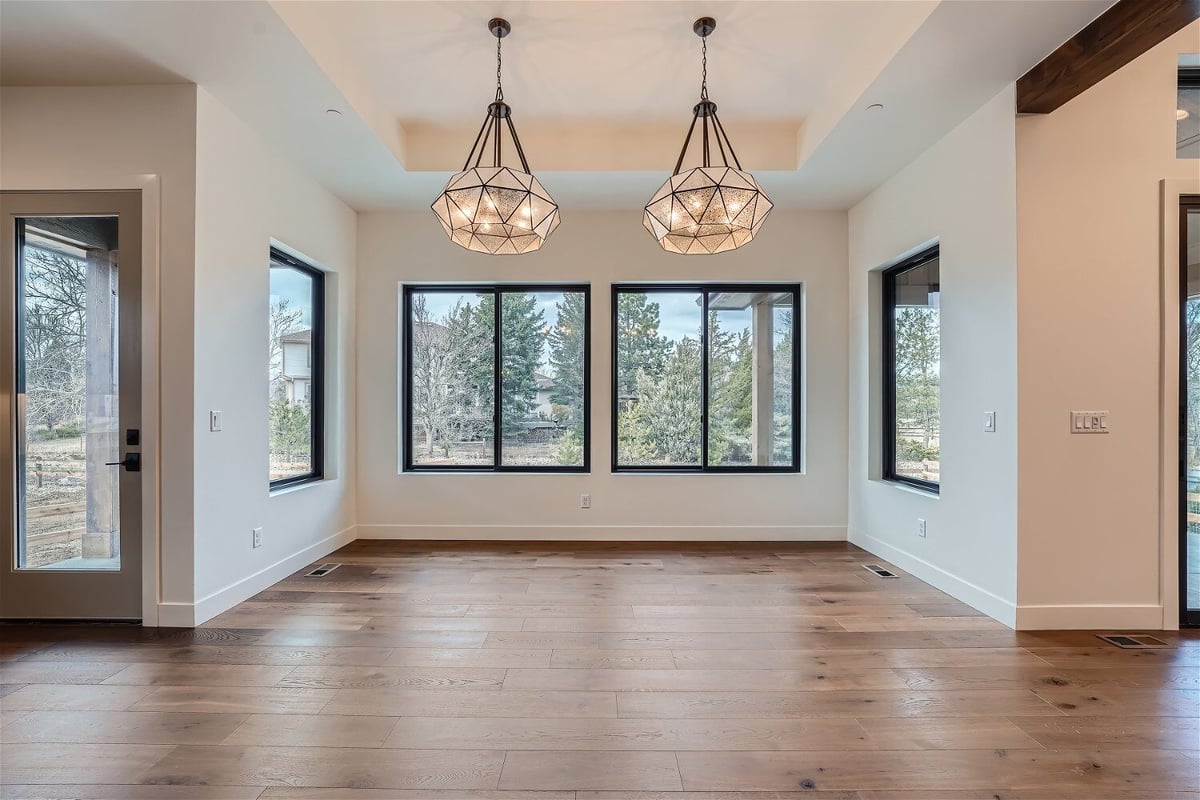 Twin chandeliers with lit bulbs in a dining room, with sliding windows in the background, by Sheffield Homes, Westminster, CO