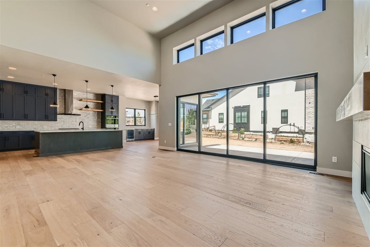 Living room with vinyl flooring, large sliding doors, and a modern open kitchen by Sheffield Homes in Westminster, CO