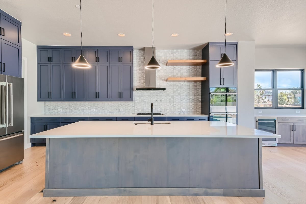 Modern kitchen with elegant lighting, solid color cabinetry, and a storage closet by Sheffield Homes in Westminster, CO