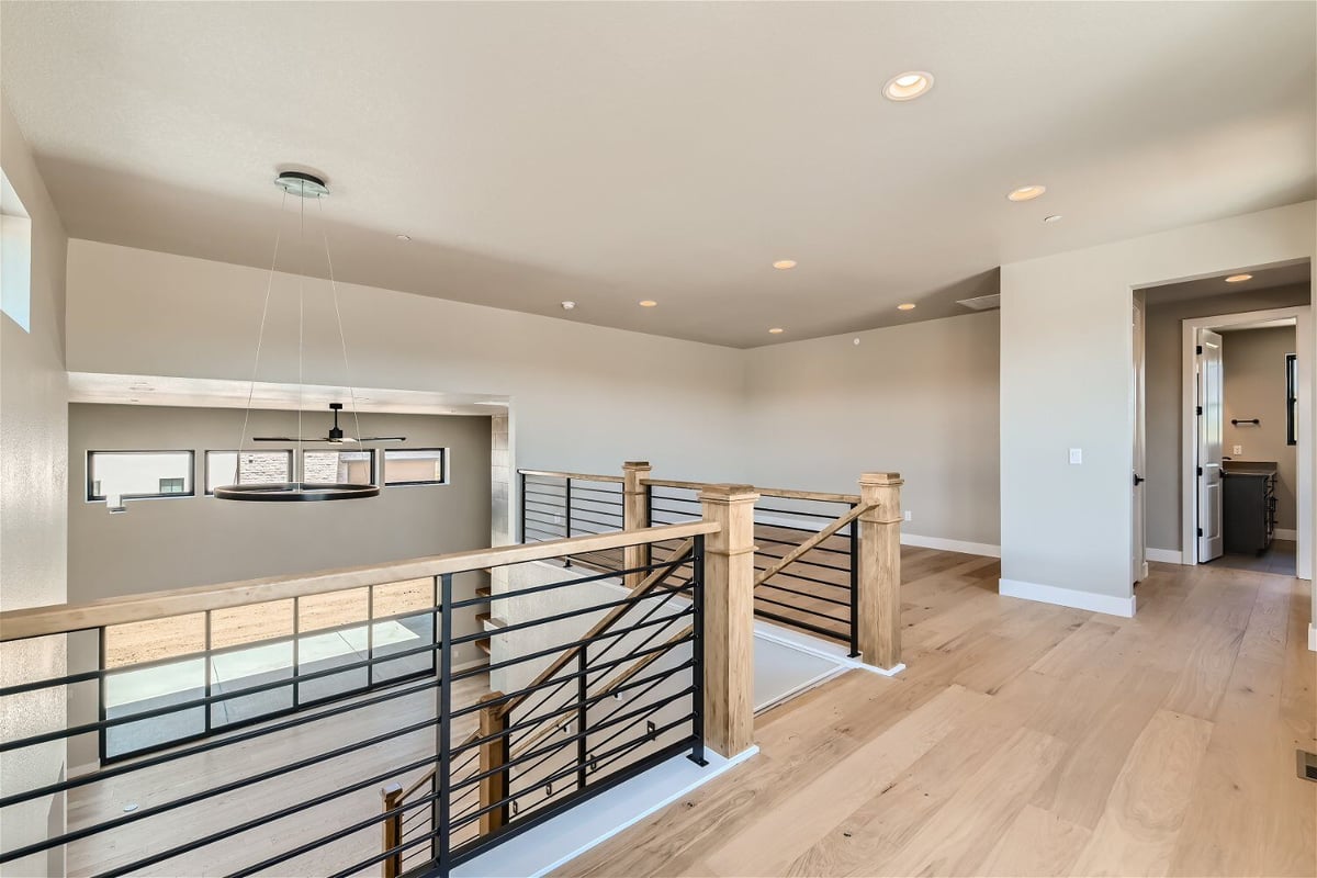 Second-floor hallway with vinyl flooring, wooden railing and metal fence in a Sheffield Homes home in Westminster, CO