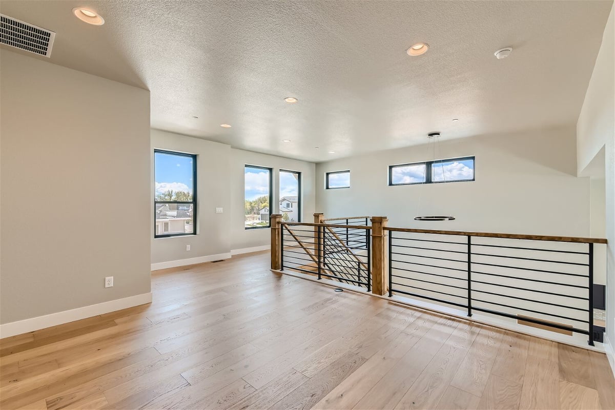 Second-floor loft with vinyl flooring, wooden railing and metal fence in a Sheffield Homes home in Westminster, CO