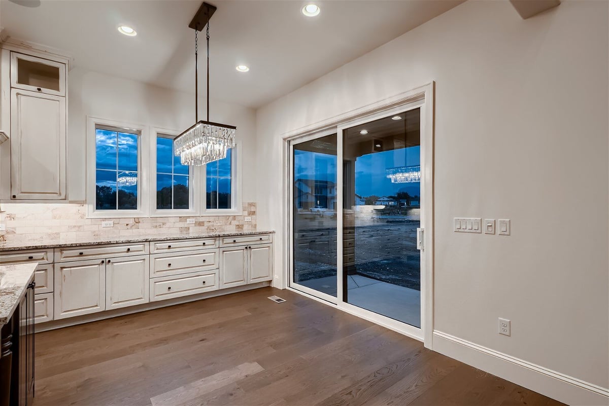 Open kitchen corner with white cabinetry and a pendant chandelier beside a door, in a Sheffield Homes home in Westminster, CO