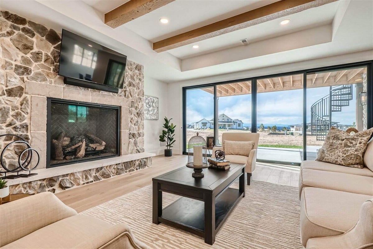 Cozy lower-level family room in a custom Denver home by Sheffield Homes, featuring a stone fireplace, rustic wood beams, and expansive sliding glass doors