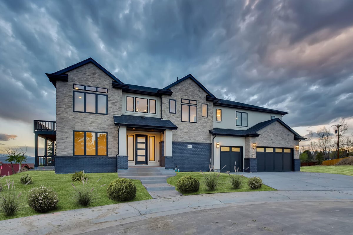 Elegant custom home by Sheffield Homes in Denver, CO, with stone facade and expansive windows, set against a dramatic evening sky