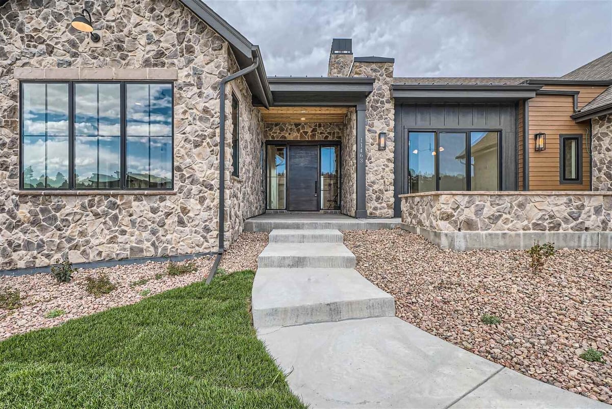 Front entry of a rustic stone-clad custom home by Sheffield Homes in Denver, CO, with modern accents and landscaped walkway