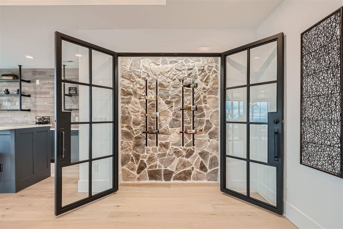 Stone-accented wine cellar in basement with glass doors, designed by Sheffield Homes in Franktown, CO